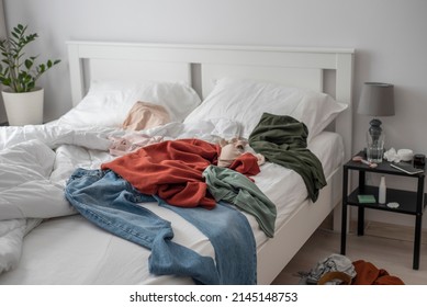 Clothes Thrown All Around The Bed. Cluttered Bedroom With A White Bedding And A Minimalistic Modern Interior.