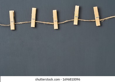 Clothesline with five wooden clothespins and rope on background of dark concrete. Space for text. Top view