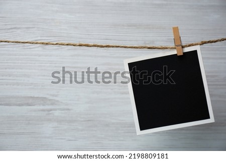 Clothespin with empty instant frame on twine against white wooden background. Space for text