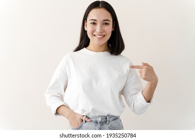 Clothing, design and advertising concept. Indoor shot of a positive young woman pointing to a copy space on her blank white t-shirt for your text or promotional content.