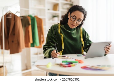 Clothing Design Software And E-Learning. Professional Designer Woman Using Laptop Computer And Taking Notes Working Online Sitting In Modern Office. Fashion Design And Tailoring Concept