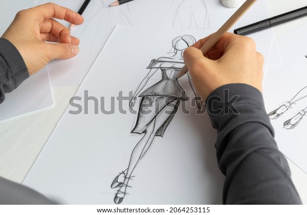 Clothing\
designer draws sketches on paper in the workplace. The artist\
creates a model for the dress. Fashion\
concept.