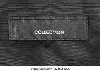 Clothing label says collection stitched on black fabric background closeup