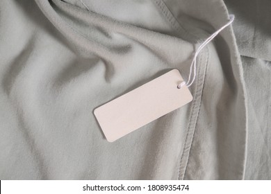 Clothing Paper Tag On Ligh Gray Fabric. Fashion Brand Name Mock Up, Closeup, Top View, Copy Space For Text