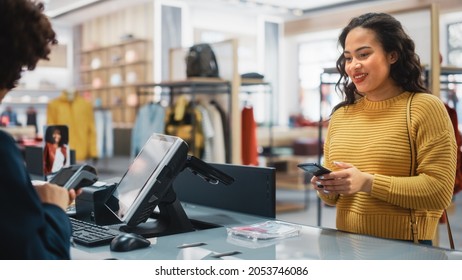 Clothing Store Checkout Cashier Counter: Woman Retail Sales Manager Accept NFC Smartphone and Credit Card Payments from a Young Female Customers for Clothes. - Shutterstock ID 2053746086