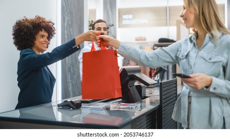 Clothing Store Checkout Cashier Counter: Woman And Male Retail Sales Managers Accept NFC Smartphone Payment From A Young Stylish Female Customer For Clothes And Pass A Recyclable Bag.