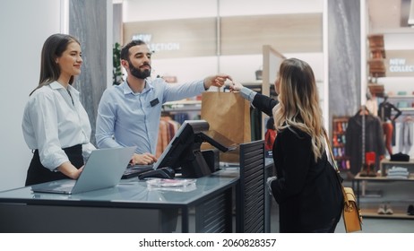 Clothing Store Checkout Cashier Counter: Beautiful Young Woman Buys Blouse From Friendly Retail Sales Assistant, Receiving Bag With Purchases. Trendy Fashion Shop With Of Designer Brands