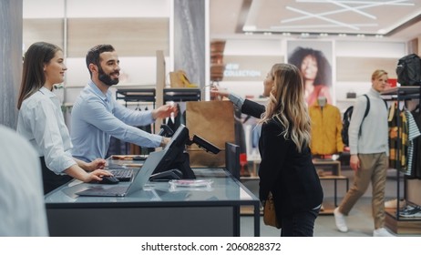 Clothing Store Checkout Cashier Counter: Beautiful Young Woman Buys Blouse From Friendly Retail Sales Assistant, Receiving Bag With Purchases. Trendy Fashion Shop With Of Designer Brands