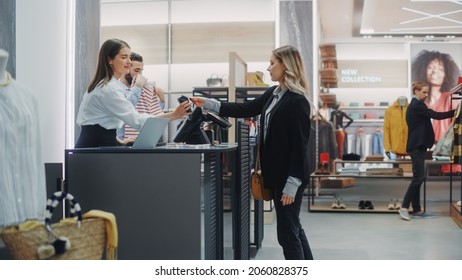 Clothing Store Checkout Cashier Counter: Beautiful Young Woman Buys Blouse From Friendly Retail Sales Assistant, Paying With Contactless Credit Card. Fashion Shop With Of Designer Brands.