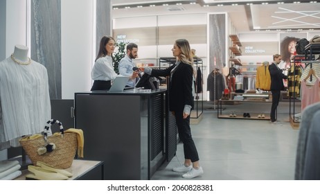 Clothing Store Checkout Cashier Counter: Beautiful Young Woman Buys Blouse from Friendly Retail Sales assistant, Paying with Contactless Credit Card. Fashion Shop with of Designer Brands. - Shutterstock ID 2060828381