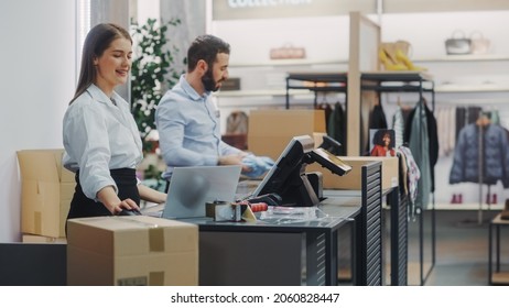 Clothing Store Checkout Cashier Counter: Female And Male Retail Sales Managers Carefully Packing Online Ordered Clothes Into Boxes. Fashionable Shop, With Stylish Brand Designs Available On Internet