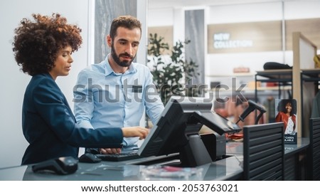 Clothing Store Checkout Cashier Counter: Female Retail Sales Manager Explaining to New Male Assistant Employee Everything He Needs to Know About Working at Fashionable Shop with Stylish Brand Designs.