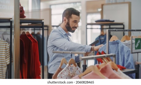 Clothing Store: Male Visual Merchandising Professional Uses Tablet Computer To Create Collection. Fashionable Shop Sales Retail Manager Checks Stock. Big Mall Supermarket With Stylish Merchandise