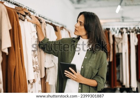 Clothing store owner conducting a stock take in her shop with the help of a trusty tablet. Focused business woman checking and counting items to ensure her inventory is accurate and up-to-date