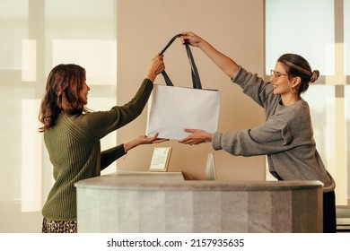 Clothing Store Owner Handing A Female Customer A Shopping Bag With Her Clothing Items. Happy Small Business Owner Assisting An Online Shopper During An In Store Collection.