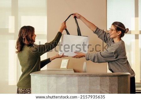 Clothing store owner handing a female customer a shopping bag with her clothing items. Happy small business owner assisting an online shopper during an in store collection.