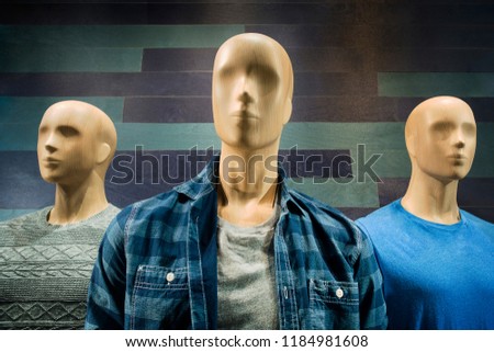 clothing store window with three maile manicans heads and torso with clothing bold wooded grained heads with generic faces