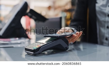 Clothing Store: Woman At Counter Buys Clothes Paying with Smartphone Through, Contactless NFC Terminal. Department Store, Shopping Center, Mall Purchase. Close-up Focus on Mobile Phone
