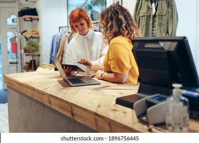 Clothing store workers standing at checkout counter using digital tablet. Two fashion shop partners looking at online orders on a tablet computer in store.