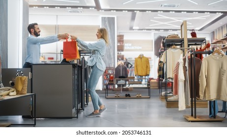 Clothing Store: Young Woman At Counter Takes Shopping Bags With Clothes From Friendly Retail Sales Assistant, Goes Away In Happy Mood, Smiling, Spinning And Dancing. Fashion Shop With Designer Brands.