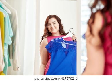 clothing, wardrobe, fashion, style and people concept - happy plus size woman with dress on hanger at mirror at home