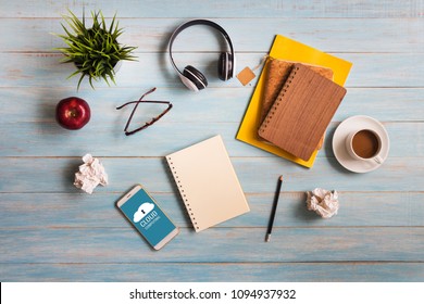 Cloud computing concept with smartphone, stationary, headphone, glasses and hot coffee on rustic blue wooden table flat lay background