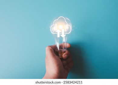 Cloud computing and innovation concept, hand holding light bulb with cloud tech icon on blue background, artificial intelligence, data storage, and future smart solutions.