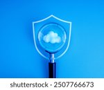 Cloud computing secure management technology, cybersecurity data system storage service concept. Shield icon protecting on white small cloud, focus in magnifying glass lens on blue background.