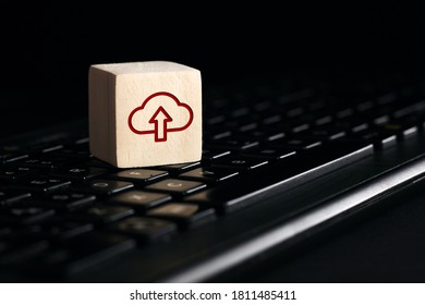 Cloud computing upload icon on wooden cube with computer keyboard against black background. Remote download technology concept.
