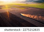 A cloud of dust rises behind a tractor plowing the ground. Spring soil preparation for sowing crops. Agrarian region of Ukraine, Europe. Aerial photography. Industry of agronomy. Beauty of earth.