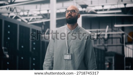 Cloud Infrastructure Architect Oversees Massive Data Center Hall. Bearded Man Overseeing Operations Inside Massive, Clean Data Center. Concept of Scale of Cloud Architecture and Big Data Management.