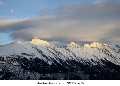 Cloud touching mountain peak at dusk with moon and a hint of sunlight