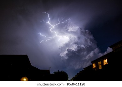 Cloud To Cloud Urban Lightning, Lighting Up House Rooftops Silhouetting In Foreground.