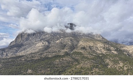 Cloudcapped mountain with dramatic sky, thick fog hugging summit, rugged rock faces, scattered pine below,