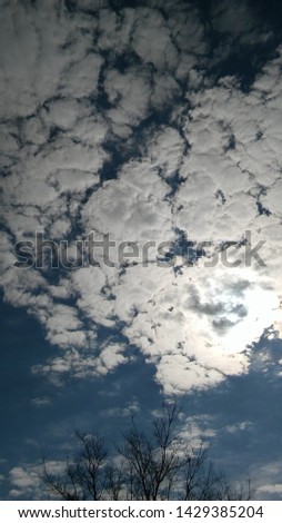 clouds in the blue sky blocking the bright sun with a black tree peeking from the buttom