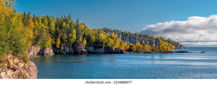 As clouds build over Lake Superior, the fall colors of the Minnesota northwoods shine bright against the rugged coast.