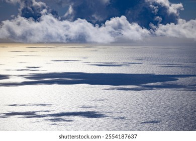 Clouds casting soft shadows over a shimmering ocean surface, creating a tranquil and atmospheric seascape . 
