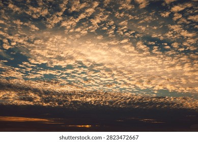 Clouds fill sky during sunset with mix of colors and patterns over horizon in evening.  large expanse  sky shows clouds during sunset. colors shift from blues to soft oranges. Light plays across clouds