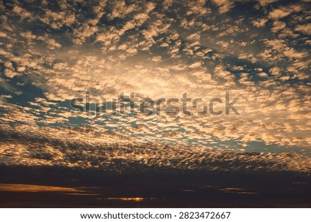 Clouds fill sky during sunset with mix of colors and patterns over horizon in evening.  large expanse  sky shows clouds during sunset. colors shift from blues to soft oranges. Light plays across clouds