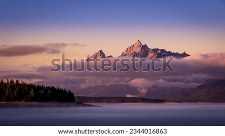 Clouds hanging over Jackson Lake as the sun rises and lights up the tallest peaks of Grand Teton National Park, Wyoming, USA