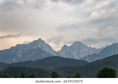 Clouds hover over a stunning mountain range in the distance, shadowing the green valley below as the day comes to a close, creating a serene and breathtaking atmosphere.
