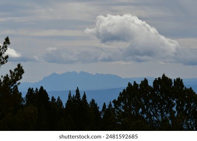 The clouds hovering over distant trees and a mountain range