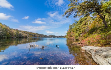 Clouds Are Reflected In A Calm Minnewaska Lake In Orange County, NY, Surrounded By Bright Fall Foliage On A Partly Cloudy Afternoon