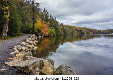 Clouds Are Reflected In A Calm Minnewaska Lake In Orange County, NY, Surrounded By Bright Fall Foliage On A Partly Cloudy Afternoon