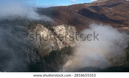 Clouds resting on the cliffs of a mellow mountain in the autumn, rainbow on the clouds