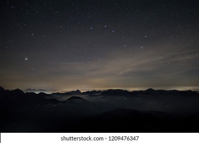 Clouds rolling over the mountains of the alps at night time with a starry sky and the constellation Big Dipper