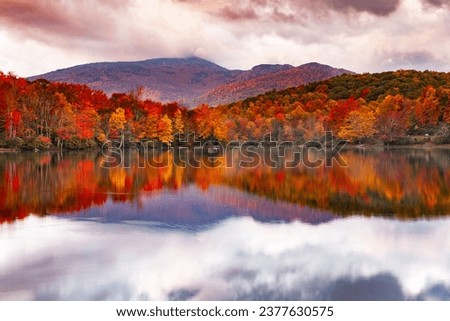 Clouds in the sky reflecting in the water of Price Lake which is lined with autumn colored trees at the base of Grandfather mountain off the Blue Ridge Parkway.