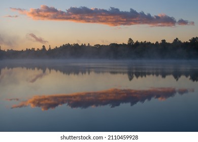 clouds at sunrise or sunset reflecting in calm tranquil water of cottage lake on holiday in northern Ontario in cottage country symmetrical shapes room for type horizontal format  background backdrop