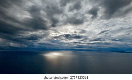 Clouds and sunset over the sea. Dramatic sunset glows through heavy storm clouds over vast ocean horizon. Golden sunlight pierces dark sky creating serene and powerful seascape.