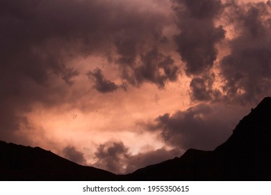 Cloudscape. Dramatic sky with colorful clouds and the mountains dark silhouette at sunset. 